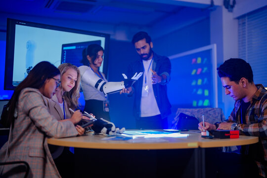 Robotics researchers debating across the prototype covered table splitting the follow up tasks components and tools under the cool lab light a natural unposed moment of office teamwork.