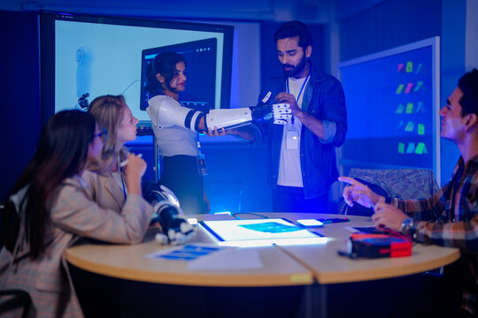 Two researchers manipulating a raised robotic arm as colleagues watch verifying the mounted sensor cool blue light washing over the research lab captured in an authentic working moment.