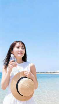 明るい海辺で水筒と帽子を持つ日本人女性