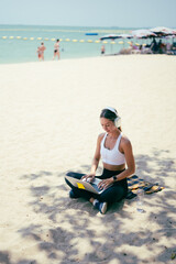 Fototapeta premium Side view of fit woman using laptop while sitting on the sand at a tropical beach