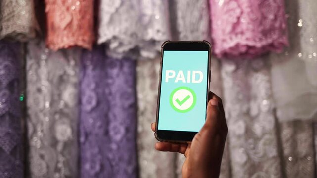 African entrepreneur successfully processing a digital payment on a smartphone in a textile shop