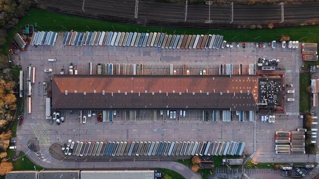 Top-down aerial view of a large industrial warehouse with logistics delivery vans lined up in rows, UK.