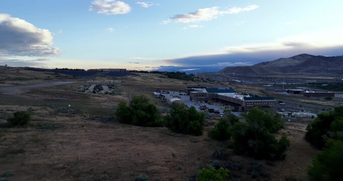 Drone pullback reveal from Camp Williams atop a hill in Lehi, Utah at sunrise, revealing rugged terrain, morning sky, valley, distant mountains, and open natural landscape.