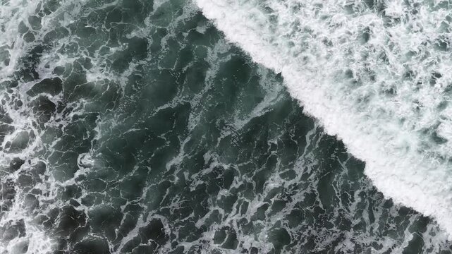 Aerial view of ocean waves crashing onto dark coastline, dynamic water movement