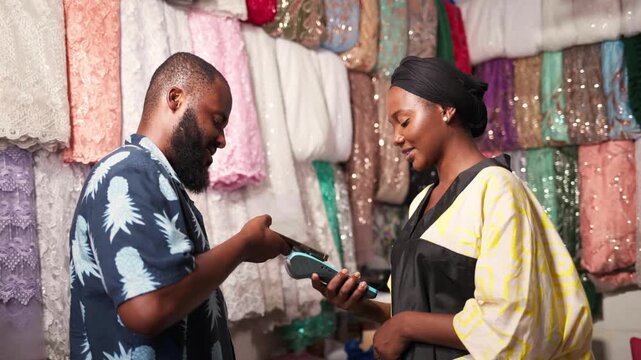 African woman small business owner processing contactless mobile payment for happy male customer in her garment shop