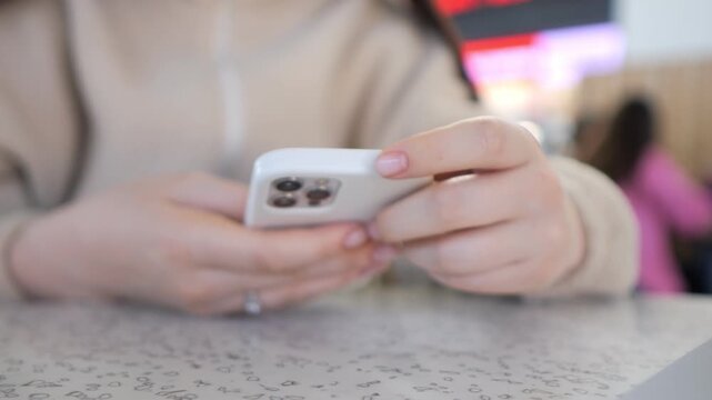 Close-up hands holding phone, focused on screen. Person seated at table, blurred background. Casual, everyday moment, modern technology use. Ideal for ads, social media, or lifestyle content