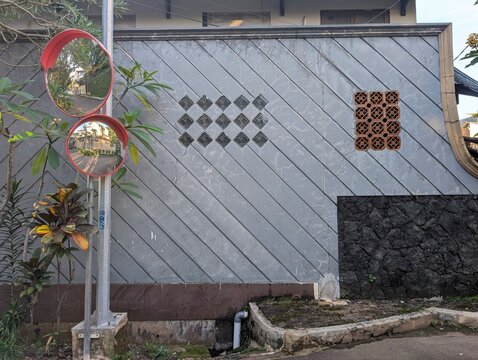 Two convex traffic safety mirrors on a pole beside a decorative grey wall with glass blocks on a residential street corner.