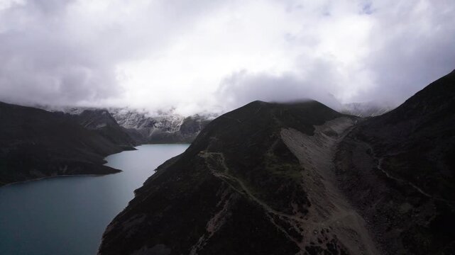 Drone view of Baimalincuo lake in Mount Kula Kangri in rainy day, well-built hiking trail circling its shore. 4k real time footage travel concept b roll shot.