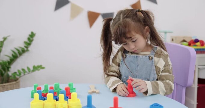 Asian preschool girl hold red peg piece, place on board, count color order, Montessori learning toy, daycare playroom, daylight window, fine motor practice, attentive study concept, skill growth.