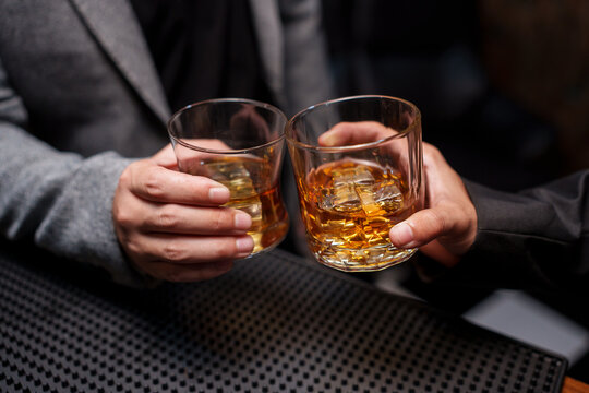 Clinking Glasses of Whiskey at a Dark Bar Counter