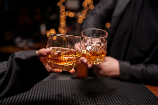 Clinking whiskey glasses in a bar at night.
