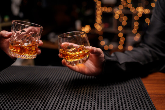 Clinking Glasses of Whiskey at a Dark Bar Counter