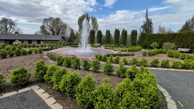 Peaceful video of a decorative fountain bordered by patterned gravel paths, lush plants and bright blue skies, capturing a relaxing spring garden setting.
