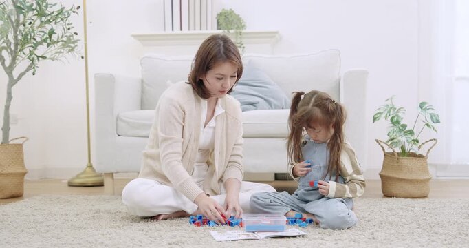 Asian single mother leaning closer, handing blocks to preschool daughter, counting aloud, correcting mistakes gently, encouraging problem solving, building trust during livingroom learning game.