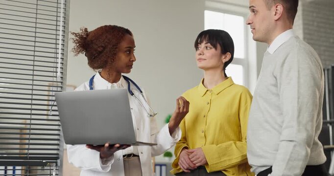 Doctor meets couple for pregnancy planning consultation. A caring doctor provides advice, test options and timelines on a laptop at the healthcare clinic for fertility. Clear family planning concept.