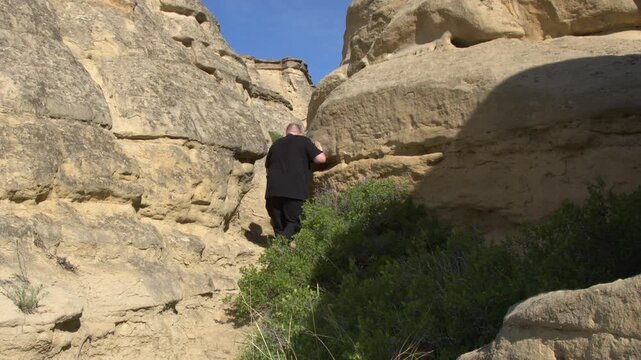 Middle aged man in black walks narrow path between sandstone hoodoos