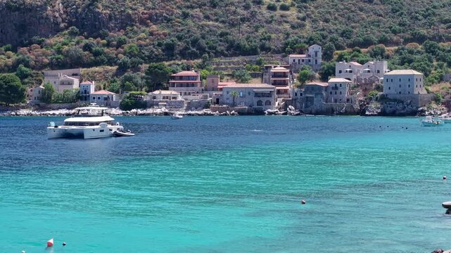 Yachting in the crystalline turquoise waters of sun drenched Limeni village on Mani Peninsula with steep hills, seaside stone tower houses in the backdrop in summer daylight, Drone shot