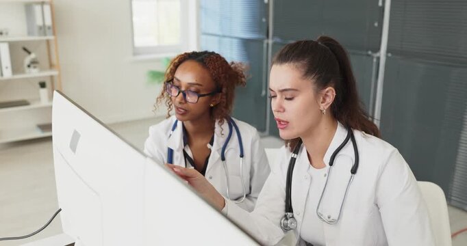 Doctors show teamwork at computer in clinic. They review healthcare data for consultation and diagnosis, updating records and documentation. Clinical teamwork and thorough analysis concept.