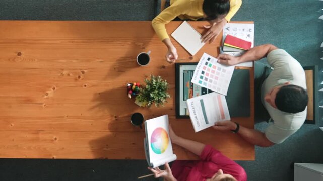 Top aerial view of business people working together to choosing color from color palette. Manager present idea by using tablet to marketing team while business man looking at logo graphic. Symposium.