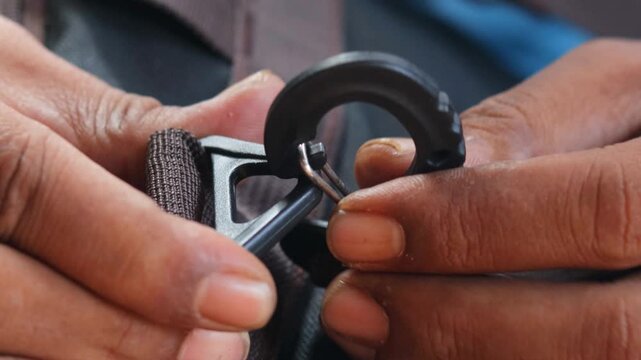 Close-up of hands attaching a plastic strap hook to a backpack strap. Connecting a replacement bag hook for backpack repair, adjustment, and everyday use.