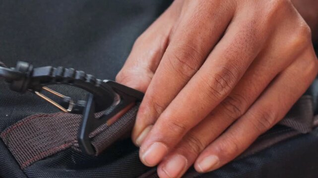 Close-up of hands attaching a plastic strap hook to a backpack strap. Connecting a replacement bag hook for backpack repair, adjustment, and everyday use.