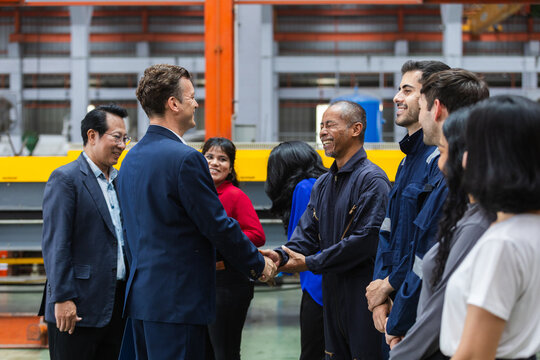 Diverse business team having happy meeting and agreement with factory worker and manager during handshake in manufacturing facility representing success