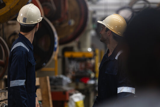 serious man worker engineer wearing safety hardhat and coverall performing inspection of heavy factory machinery during routine industrial maintenance task