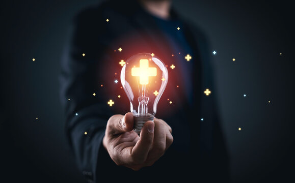 Businessman holding glowing lightbulb with plus sign mark for value added , It is symbol of business profit growth , health insurance , benefit and economy development concept