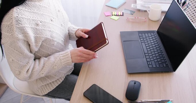 Productive work. Idea development. Unrecognizable woman manager preparing for occupation at office desk with laptop writing in notebook.