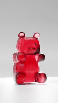 Red gummy bear candy character bouncing on floor in playful 3d animation with glossy jelly texture on minimal background. 