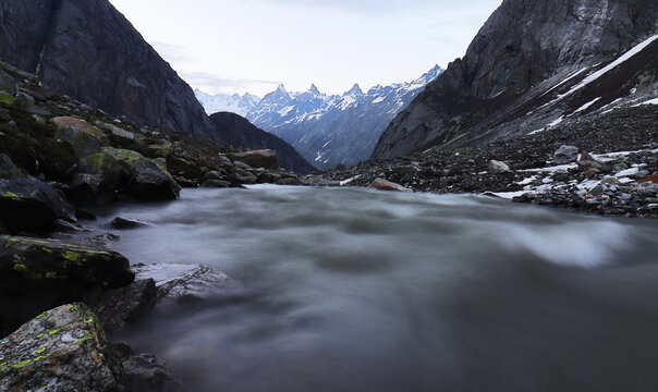 scenic view of flowing mountain stream and surrounding snowcapped himalayas from shea goru camping site in lahaul valley, hampta pass trek, adventure travel in himachal pradesh, india