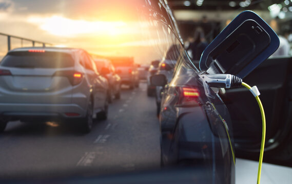 Electric car charging cable with sunset traffic jam background, composite image.