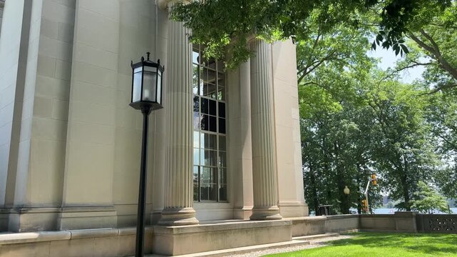 Architectural detail MIT campus in Cambridge, Massachusetts, showing a neoclassical building facade with tall fluted columns, a window bay, and a tree-lined riverside setting on a bright summer day.