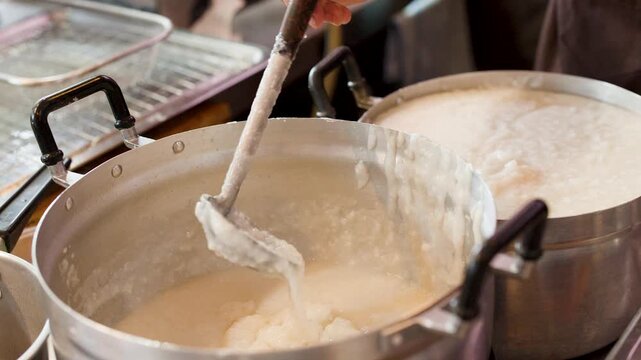 Chef Stirring Hot Rice Congee in Large Metal Cooking Pot