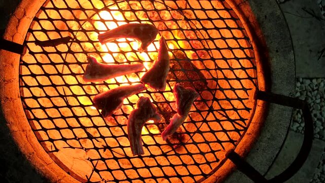 View above round glowing fire pit with juicy lamb chops being grilled over coals