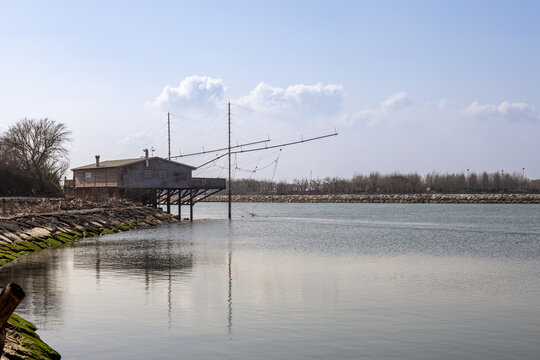 Traditional Italian fishing hut on stilts with bilancia net structure reflected in calm water at Brenta-Bacchiglione river mouth, Chioggia, Veneto, Italy