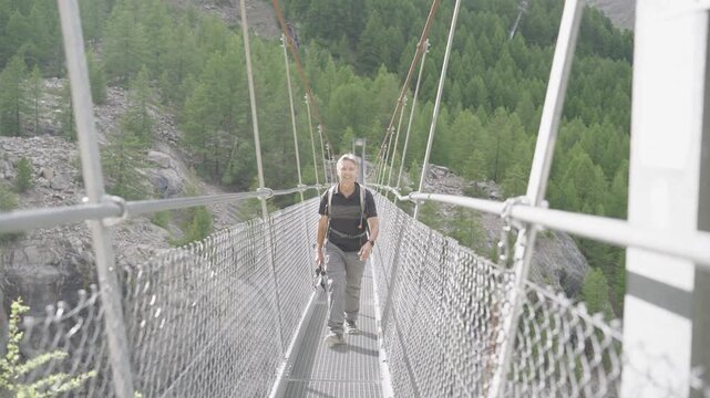 Senior man walking across a long suspension bridge high up in the swiss alps near zermatt