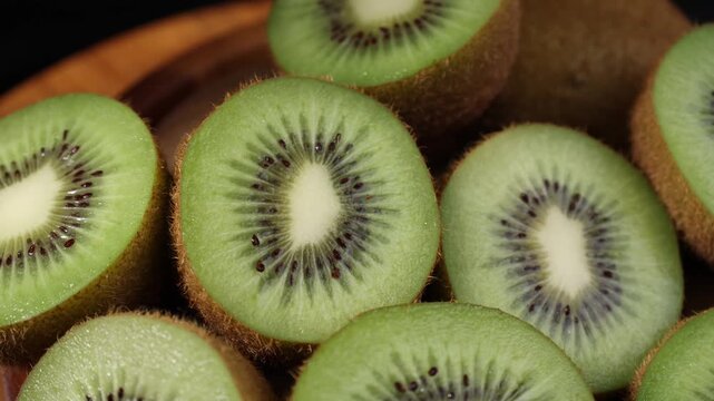 Close-up of fresh kiwi fruits arranged on a wooden table. Whole and sliced kiwis showing their vibrant green flesh and tiny black seeds under natural light. Ideal for themes of healthy eating, fresh f