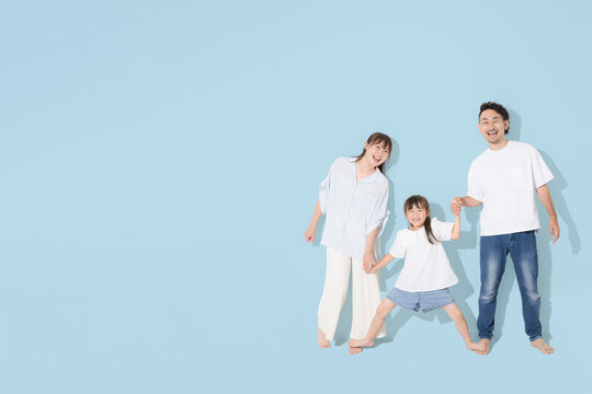 水色背景で仲良し笑顔の家族・幸せなファミリーライフと健康的な暮らし　保険やnisaなど教育や成長　全身で手を繋ぐ　広角のコピースぺースあり半袖夏イメージ