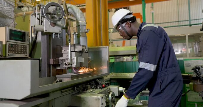 African adult male operator manages grinding machine in slow motion as spark emerges from metalworking area, depicting safe process, equipment control, production monitoring, workshop operation.