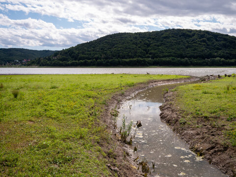 Small inflow at Doma&scaron;a reservoir near Petejovce during drought. Low water level exposed the lakebed, now covered with grass, showing the impact of prolonged dry weather.