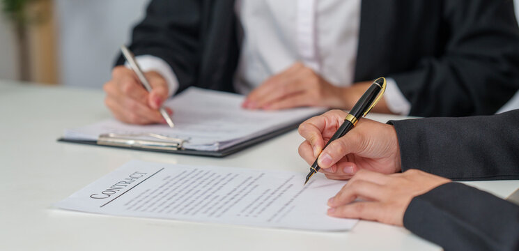 Cropped hands of business partners signing legal contract document in office