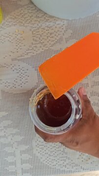 Hand scooping organic honey from a glass jar with a plastic spoon