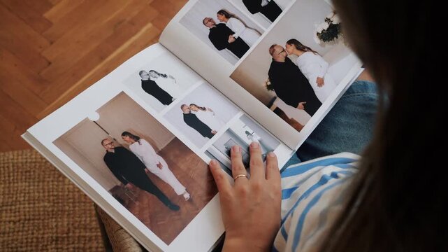 Close view of a person in casual clothes slowly flipping through a wedding photo album while seated indoors.
