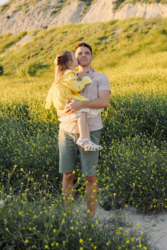 Father carrying daughter outdoors in a flower field and golden sunlight.