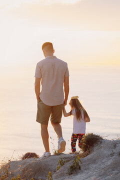 Father with daughter on seaside cliff during golden hour family vacation.