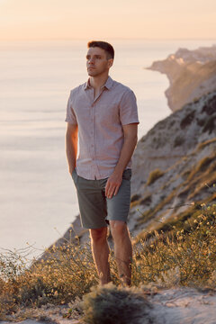 Handsome man standing near coastal rocks with ocean background in warm evening light.