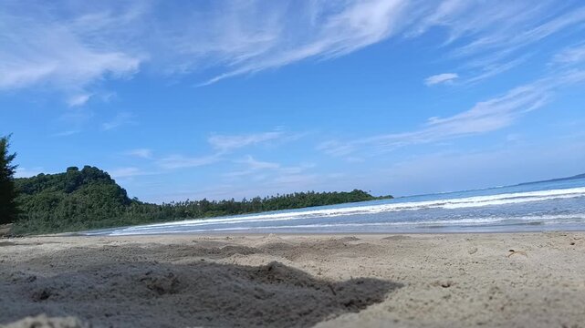 Low angle view of a tropical beach with rolling waves, clear sand, and blue sky on a sunny day