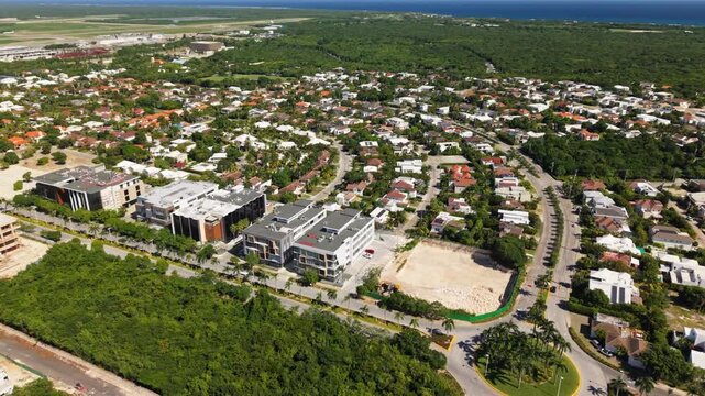 High-altitude drone shot of Punta Cana Village, highlighting integrated residential blocks, modern corporate offices, and urban layout. Aerial perspective shows tropical coastal environment