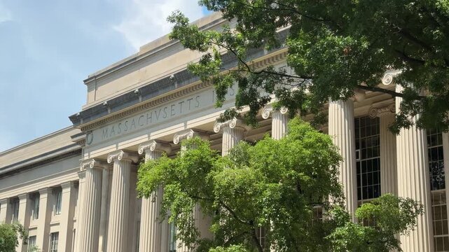 Vew of MIT&rsquo;s Building 10, Great Dome area on the Cambridge campus, with the classical columns and the carved &ldquo;Massachusetts&rdquo; inscription partially visible through the trees.